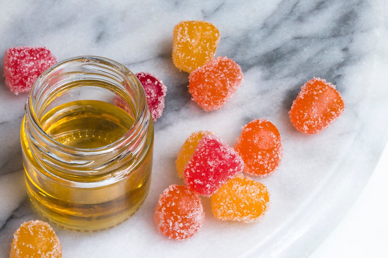 CBD gummies on a marble counter next to CBD oil.