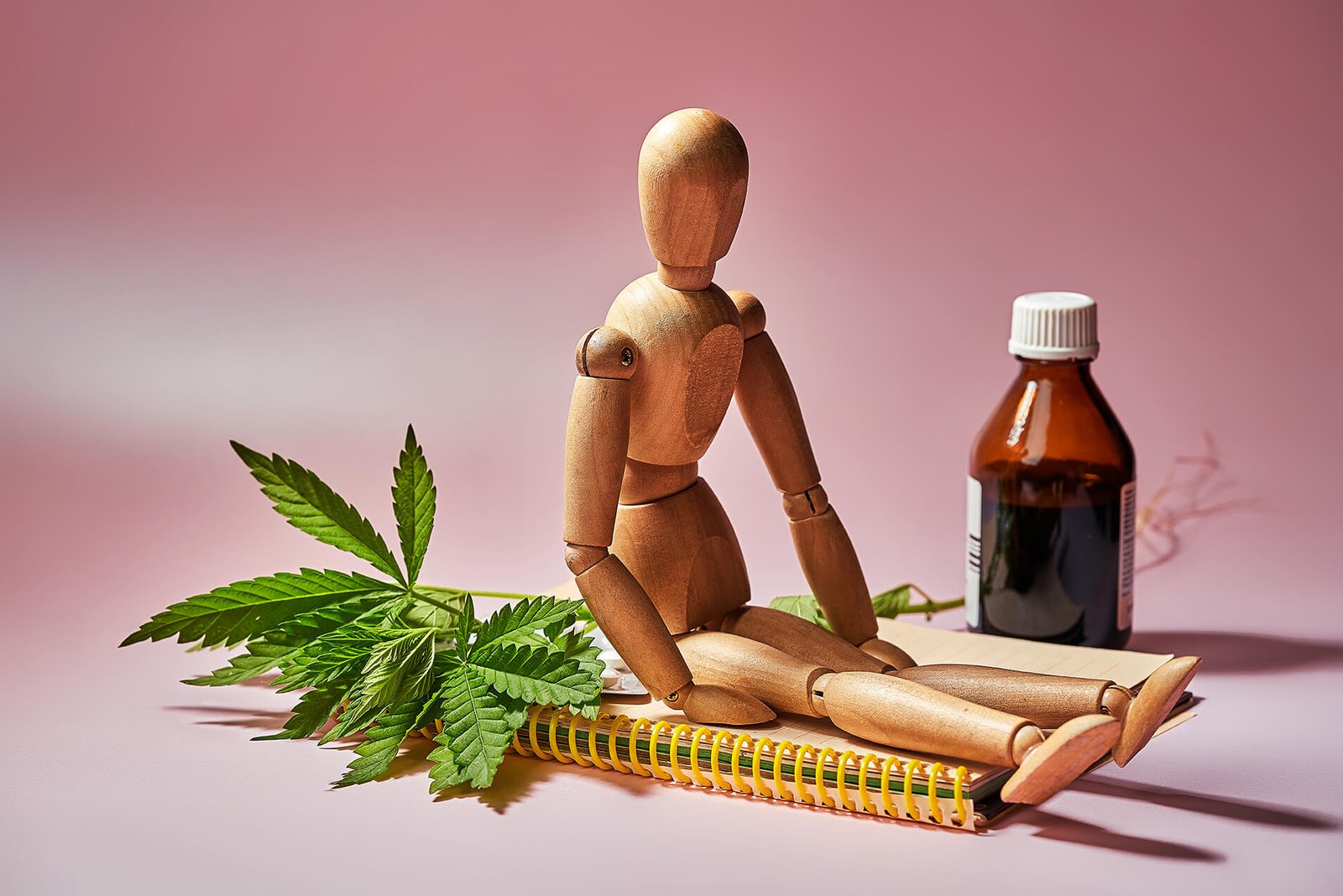 Wooden man sitting next to notepad, hemp, and CBD oil in a glass bottle.