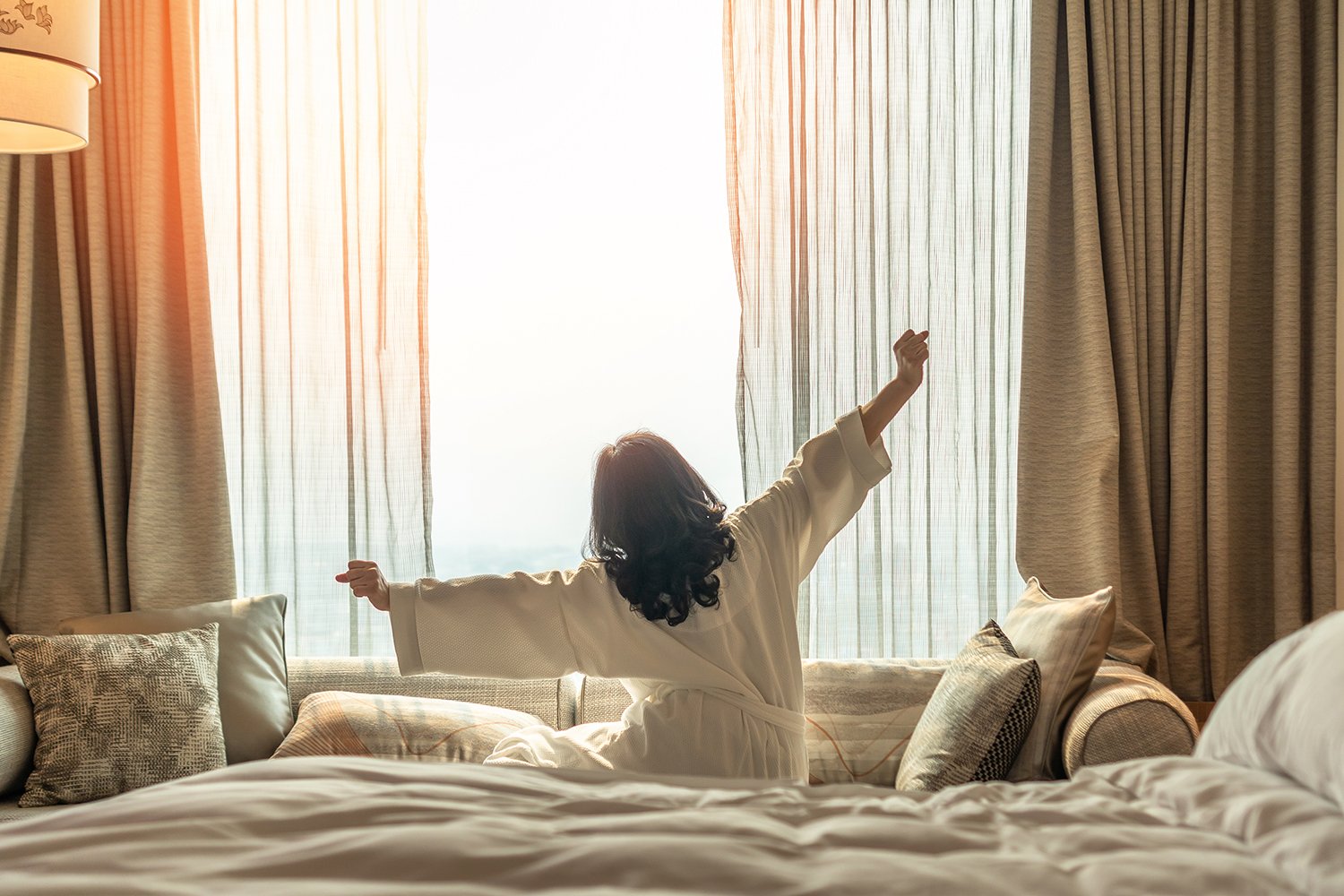 Woman waking up, stretching, and looking out the window after experiencing a possible benefit of CBD for relaxation.