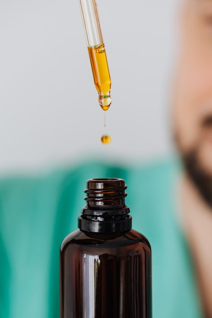 Detailed view of a pipette dropping CBD oil into an amber glass bottle.