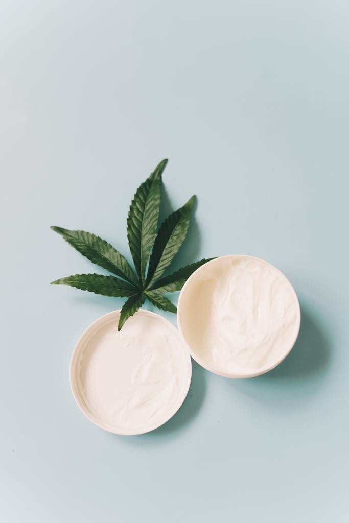 Top view of CBD skincare cream with hemp leaf on light blue background.