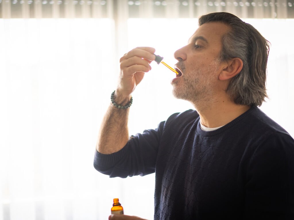 Mature man taking CBD oil under tongue - Alternative medicine concept