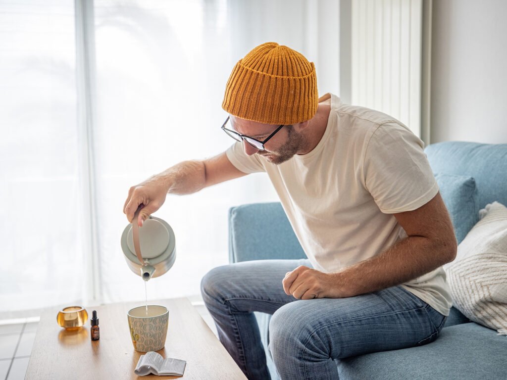 Young man using CBD for anti-inflammatory relief at home, he uses some CBD oil in a tea.