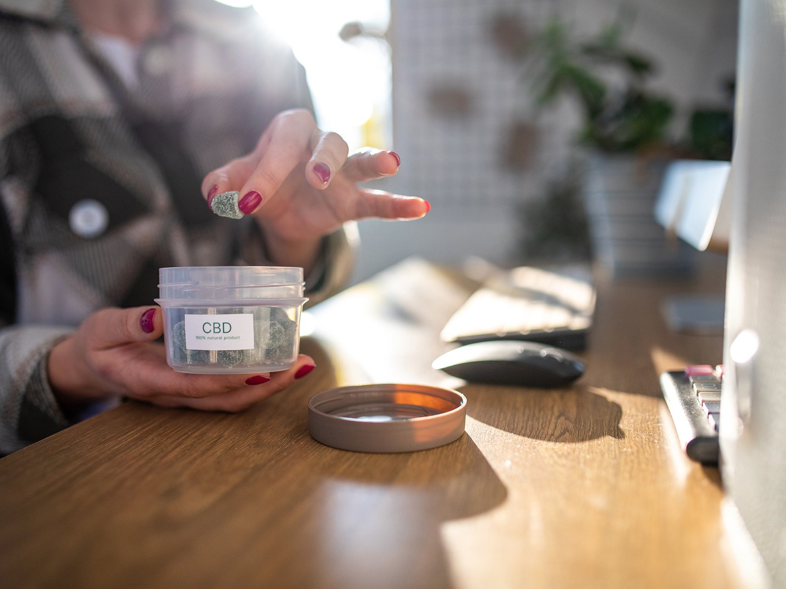 Woman working in her home work space. She is opening a CBD full-spectrum gummy candy to take a snack.