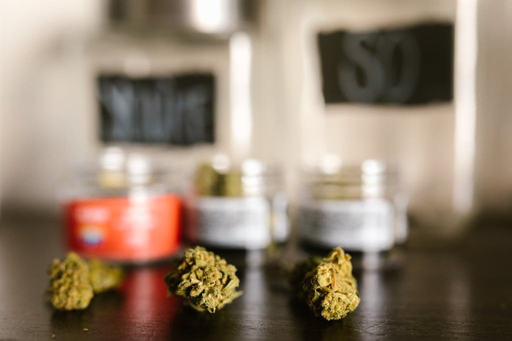 Macro shot of cannabis buds with blurred glass jars in the background, emphasizing texture and color.
